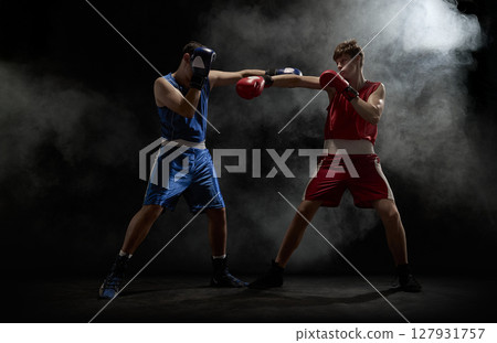 Boxers in blue and red engage in intense fight amidst smoke on dark background Boxers in blue and red engage in intense fight amidst smoke on dark background 127931757