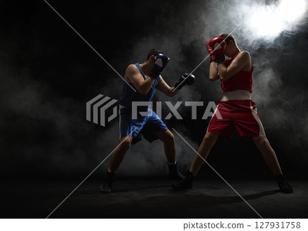 Two boxers sparring in dramatic smoke-filled arena atmosphere Two boxers sparring in dramatic smoke-filled arena atmosphere 127931758