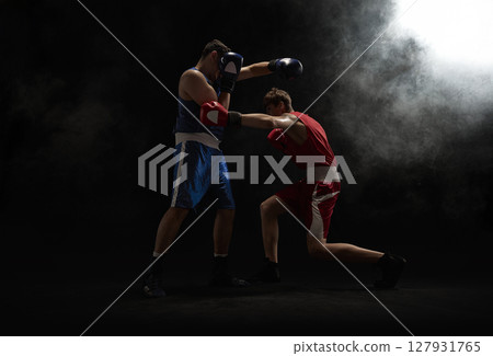 Two boxers in action during intense match with dramatic lighting and dark smoky background 127931765