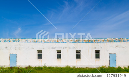 Abandoned white building with peeling paint in rural field 127931949