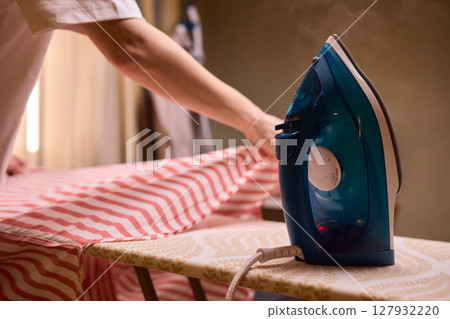 A person meticulously ironing clothes at home, ensuring all garments are neat and well cared for 127932220