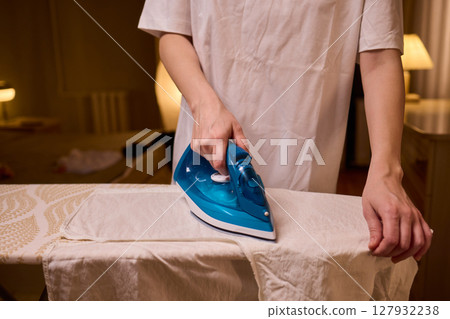 A person meticulously ironing clothes at home, ensuring all garments are neat and well cared for 127932238