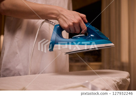 A person meticulously ironing clothes at home, ensuring all garments are neat and well cared for A person meticulously ironing clothes at home, ensuring all garments are neat and well cared for 127932246