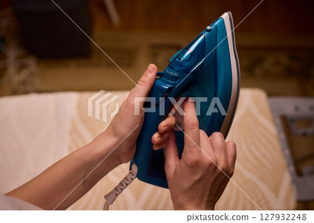 A person meticulously ironing clothes at home, ensuring all garments are neat and well cared for A person meticulously ironing clothes at home, ensuring all garments are neat and well cared for 127932248