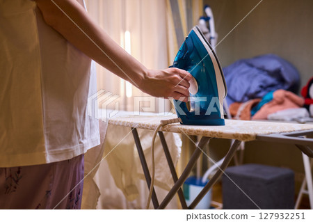 A person meticulously ironing clothes at home, ensuring all garments are neat and well cared for 127932251
