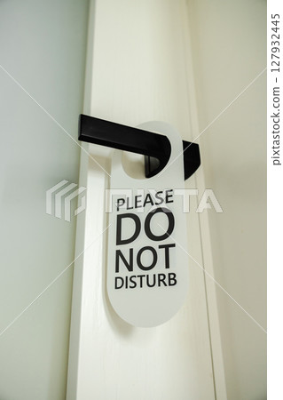 Modern black door handle with a white hanging sign that reads Please Do Not Disturb in bold black letters 127932445