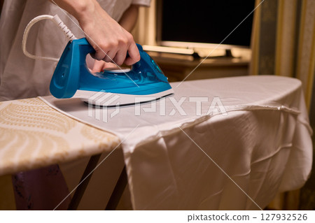 A person meticulously ironing clothes at home, ensuring all garments are neat and well cared for A person meticulously ironing clothes at home, ensuring all garments are neat and well cared for 127932526