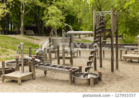 Children's playground showcases various metal play equipment designed for physical activity and exploration, set in a grassy area surrounded by trees during daylight Children's playground showcases various metal play equipment designed for physical activity and exploration, set in a grassy area surrounded by trees during daylight 127933357