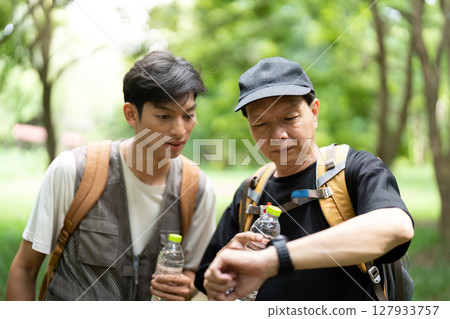 Father and Son Checking Time on Hike. A father and son pause to check their progress during an outdoor adventure. Father and Son Checking Time on Hike. A father and son pause to check their progress during an outdoor adventure. 127933757