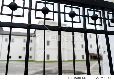 Big white Building and low sun shining seen through the gate. View through fence 127934058