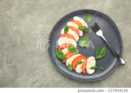 Italian Caprese salad with cherry tomatoes, mozzarella, basil on dark plate on grey concrete background. 127934130