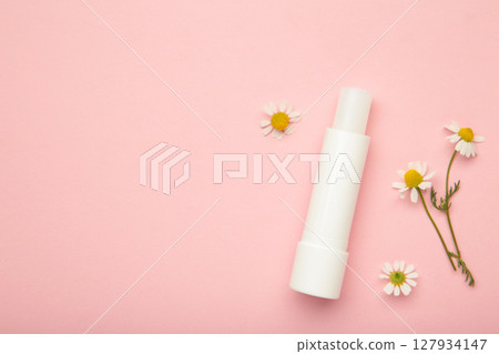 Lip balms and chamomile flowers on pink background. 127934147