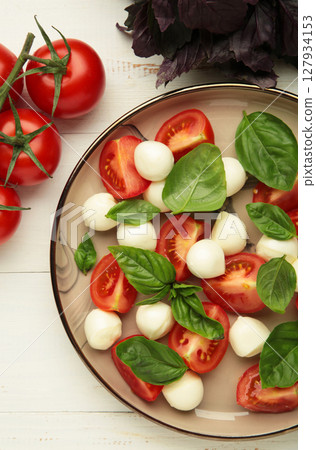 Italian Caprese salad with cherry tomatoes, mozzarella, basil on plate on white background. Vertical photo 127934153