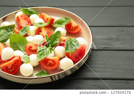 Italian Caprese salad with cherry tomatoes, mozzarella, basil on plate on black wooden background. Italian Caprese salad with cherry tomatoes, mozzarella, basil on plate on black wooden background. 127934178