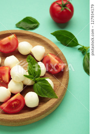 Italian Caprese salad with cherry tomatoes, mozzarella, basil on wooden plate on mint background. Vertical photo 127934179