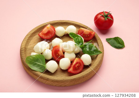 Italian Caprese salad with cherry tomatoes, mozzarella, basil on wooden plate on pink background. 127934208