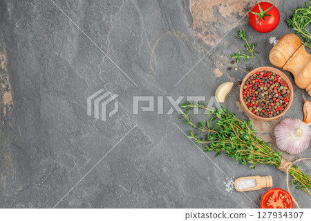 A rustic flatlay of herbs, spices, and vegetables on a dark stone background, ideal for cooking, seasoning, or Mediterranean cuisine themes 127934307
