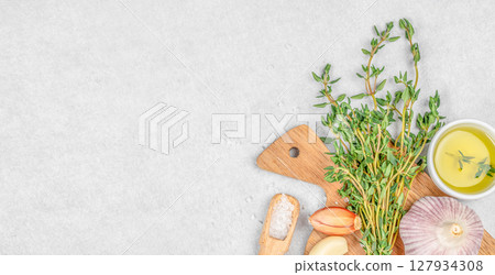 A bright culinary layout featuring fresh thyme, garlic, shallots, coarse salt, and olive oil on a light stone background, perfect for healthy cooking themes 127934308
