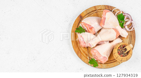 Raw chicken drumsticks arranged on a wooden board with onion rings, parsley, and peppercorns, ready for seasoning or cooking Raw chicken drumsticks arranged on a wooden board with onion rings, parsley, and peppercorns, ready for seasoning or cooking 127934319