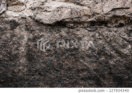Close-up of a rough, weathered stone wall featuring layered textures and earthy tones of brown, black, and gray with natural surface erosion Close-up of a rough, weathered stone wall featuring layered textures and earthy tones of brown, black, and gray with natural surface erosion 127934340