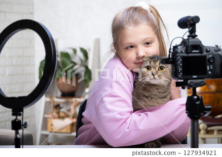 A beautiful blonde -teenage broadcasts live with her cat. Living a broadcast. Ring lamp and camera during a direct broadcast of a video -blogger 127934921