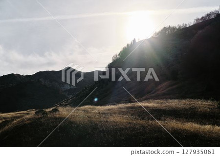 Sunlight breaks over a mountain ridge in Montenegro Prokletije National Park, illuminating dry autumn grasses and casting long evening shadows Sunlight breaks over a mountain ridge in Montenegro Prokletije National Park, illuminating dry autumn grasses and casting long evening shadows 127935061