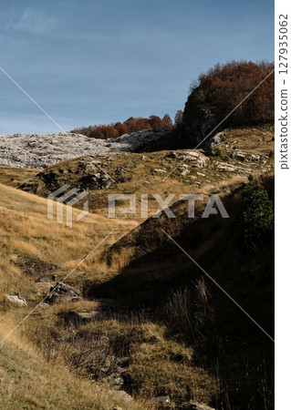 Golden grasslands and rugged rocky hills glow under warm autumn light in Montenegro country, Prokletije National Park. A scenic moment of nature raw beauty Golden grasslands and rugged rocky hills glow under warm autumn light in Montenegro country, Prokletije National Park. A scenic moment of nature raw beauty 127935062