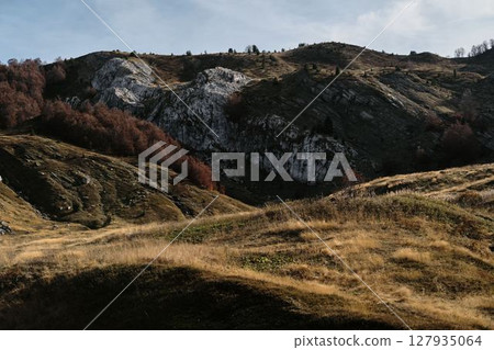 Golden grasslands and rugged rocky hills glow under warm autumn light in Montenegro country, Prokletije National Park. A scenic moment of nature raw beauty Golden grasslands and rugged rocky hills glow under warm autumn light in Montenegro country, Prokletije National Park. A scenic moment of nature raw beauty 127935064