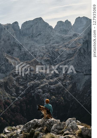 A woman hiker with a German Shepherd enjoys the breathtaking view of Montenegro Prokletije mountains in autumn season. Rear view. Travel with pet concept A woman hiker with a German Shepherd enjoys the breathtaking view of Montenegro Prokletije mountains in autumn season. Rear view. Travel with pet concept 127935069