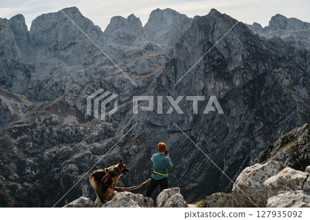 A woman photographing or making video of rugged mountains of Prokletije in Montenegro with her German and Australian Shepherd by her side, enjoying the beauty of the autumn wilderness A woman photographing or making video of rugged mountains of Prokletije in Montenegro with her German and Australian Shepherd by her side, enjoying the beauty of the autumn wilderness 127935092