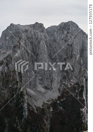 Massive gray limestone cliffs of Prokletije National Park in Montenegro rise vertically above dense forests 127935178
