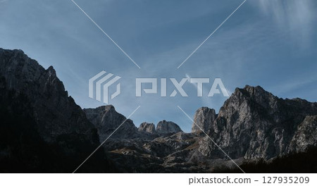 Panoramic view of jagged limestone peaks in Prokletije Mountains under soft morning light and dramatic blue sky. Nature of Montenegro country 127935209
