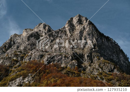 Majestic rocky mountain peak of Prokletije National Park in Montenegro rises above colorful autumn forest under clear blue sky Majestic rocky mountain peak of Prokletije National Park in Montenegro rises above colorful autumn forest under clear blue sky 127935210