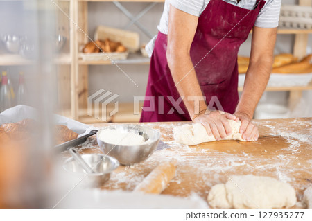 Elderly baker hands kneading dough on table, closeup 127935277