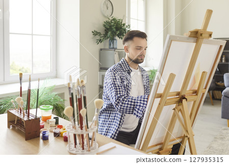An artist paints in a bright studio filled with colorful supplies and materials 127935315