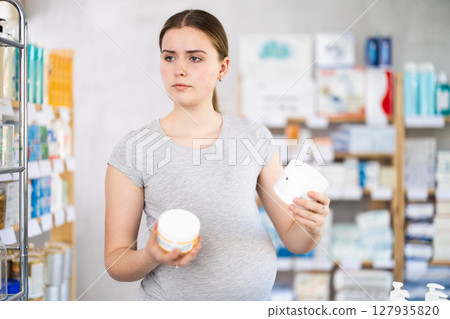 Young pregnant woman choosing cream in drugstore Young pregnant woman choosing cream in drugstore 127935820