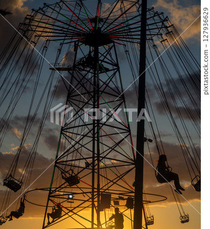 Silhouettes of people on the carousel. Concept of fun and entertainment. People on carousels at sunset. Resort town.  Adrenalin. Speed carousel 127936629