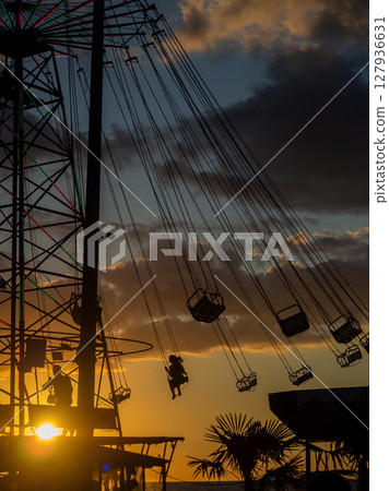 Silhouettes of people on the carousel. Concept of fun and entertainment. People on carousels at sunset. Resort town. Lunapark. Adrenalin. 127936631