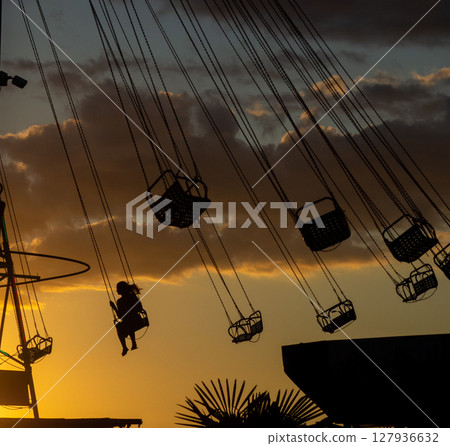 Silhouettes of people on the carousel. Concept of fun and entertainment. People on carousels at sunset. Resort town. Lunapark.  Speed carousel 127936632