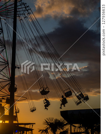 Silhouettes of people on the carousel. Concept of fun and entertainment. People on carousels at sunset. Resort town.  Adrenalin. Speed carousel 127936633