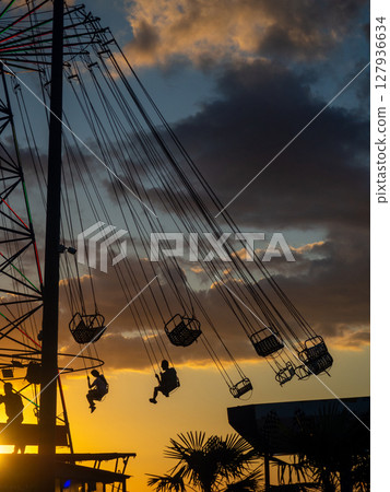 Silhouettes of people on the carousel. Concept of fun and entertainment. People on carousels at sunset. Resort town. Lunapark. Adrenalin. Silhouettes of people on the carousel. Concept of fun and entertainment. People on carousels at sunset. Resort town. Lunapark. Adrenalin. 127936634