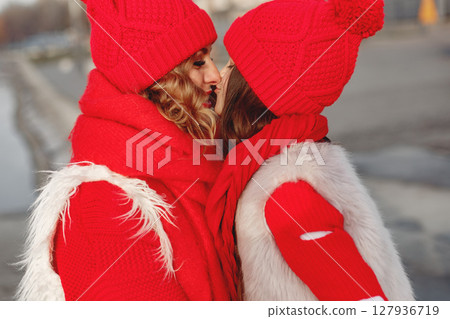 Mother and child in knitted winter hats on family Christmas vacation. Handmade wool hat and scarf for mom and kid. Knitting for kids. Knit outerwear. Woman and little girl in a park. 127936719