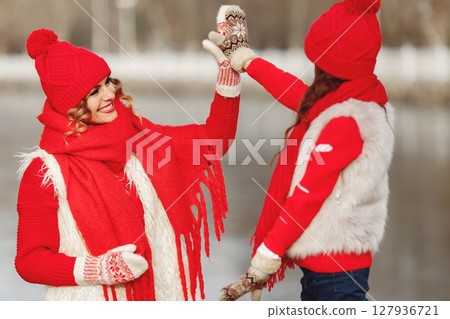 Mother and child in knitted winter hats on family Christmas vacation. Handmade wool hat and scarf for mom and kid. Knitting for kids. Knit outerwear. Woman and little girl in a park. 127936721