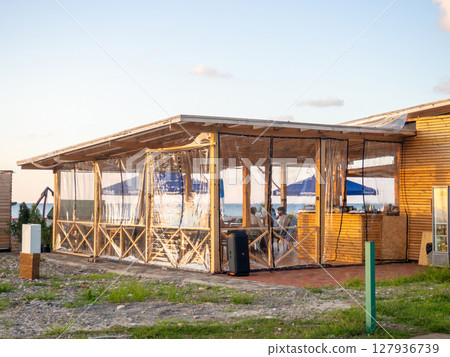 Street restaurant made of wood. Plastic curtains in the restaurant against the wind. Snack bar on the seashore. Weather protection Street restaurant made of wood. Plastic curtains in the restaurant against the wind. Snack bar on the seashore. Weather protection 127936739