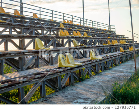 Old broken plastic chairs at the stadium. Abandoned stand at the stadium. Concept of devastation. 127936771