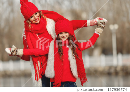 Mother and child in knitted winter hats on family Christmas vacation. Handmade wool hat and scarf for mom and kid. Knitting for kids. Knit outerwear. Woman and little girl in a park. 127936774