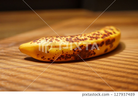 Brown-spotted banana resting on wooden surface with striped shadows during afternoon light 127937489