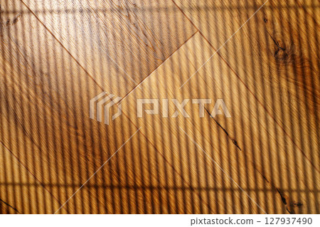 Light and shadows create patterns on wooden flooring in a sunlit room during a quiet afternoon 127937490