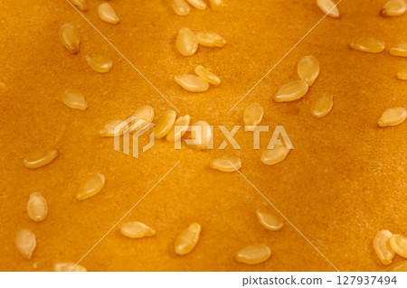 Close-up view of a hamburger bun displaying a warm golden hue, adorned with a sprinkle of sesame seeds Close-up view of a hamburger bun displaying a warm golden hue, adorned with a sprinkle of sesame seeds 127937494