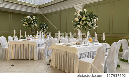 Refined wedding banquet hall interior with white tablecloths, floral centerpieces, napkin arrangements, and elegant decor, ideal for celebrations, receptions, and formal events 127937592